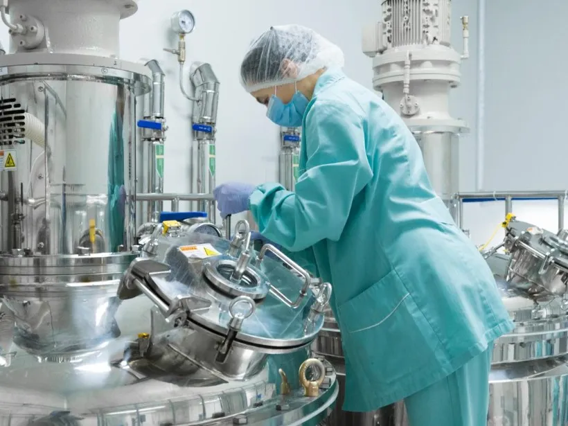 Mitarbeiterin in Schutzkleidung an einer Extraktionsanlage aus Edelstahl