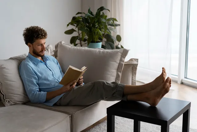 Junger Mann liegt entspannt unter einer gelben Decke auf dem Sofa