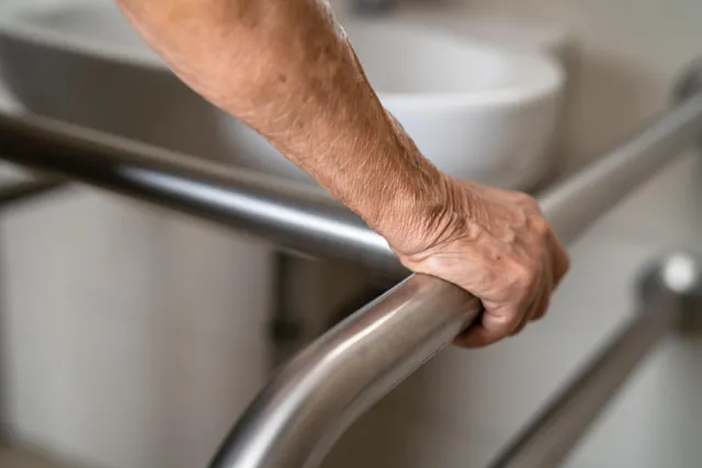 Hand einer älteren Person am Haltegriff neben einem Waschbecken im Bad