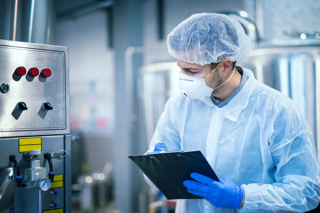 Mitarbeiter in Schutzkleidung dokumentiert Prüfwerte an einer Produktionsanlage
