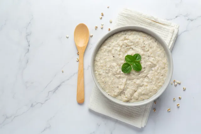 Hände schöpfen Haferbrei aus einem Topf in eine flache Schale